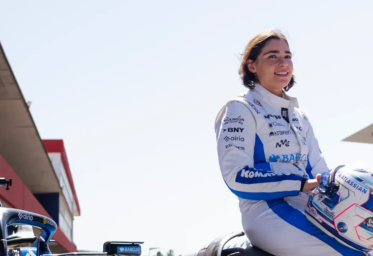 Jami Chadwick. female racing driver holds her helmet beside a race car in the pit lane.