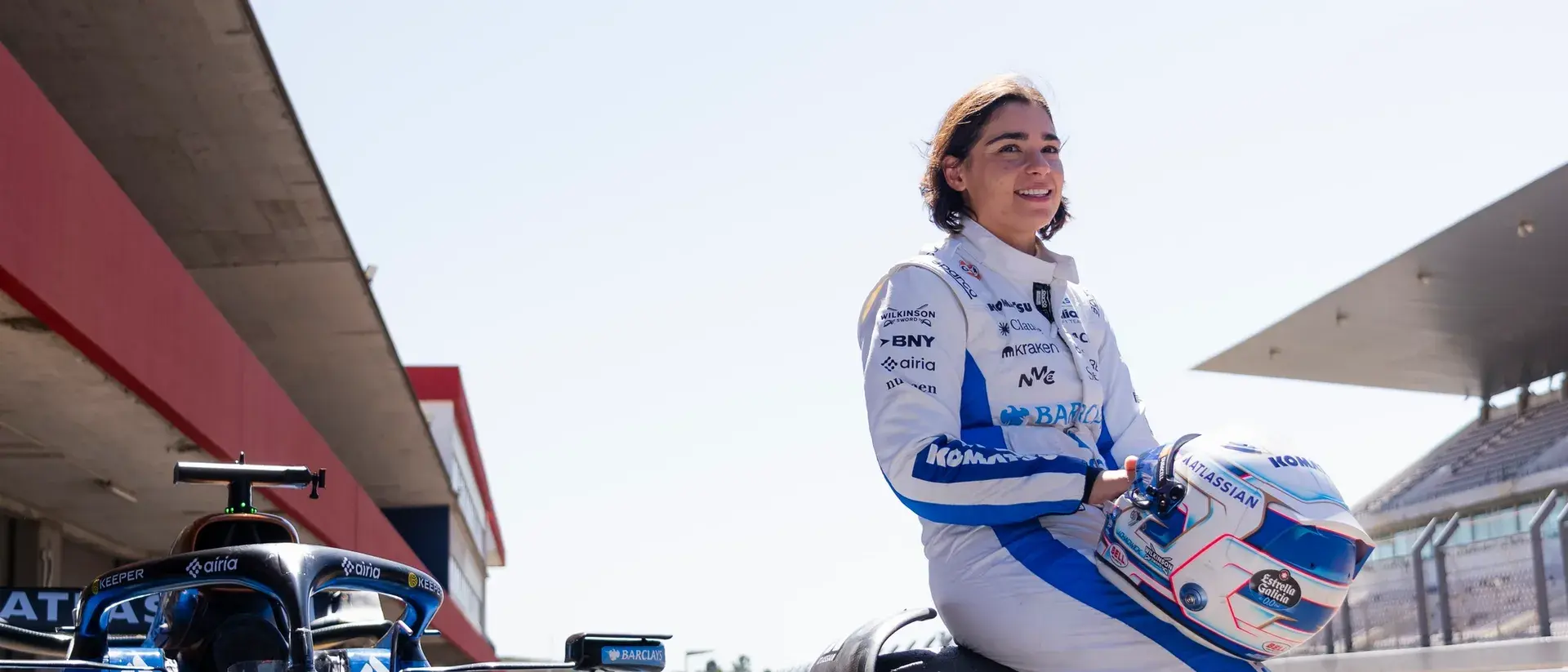 Jami Chadwick. female racing driver holds her helmet beside a race car in the pit lane.