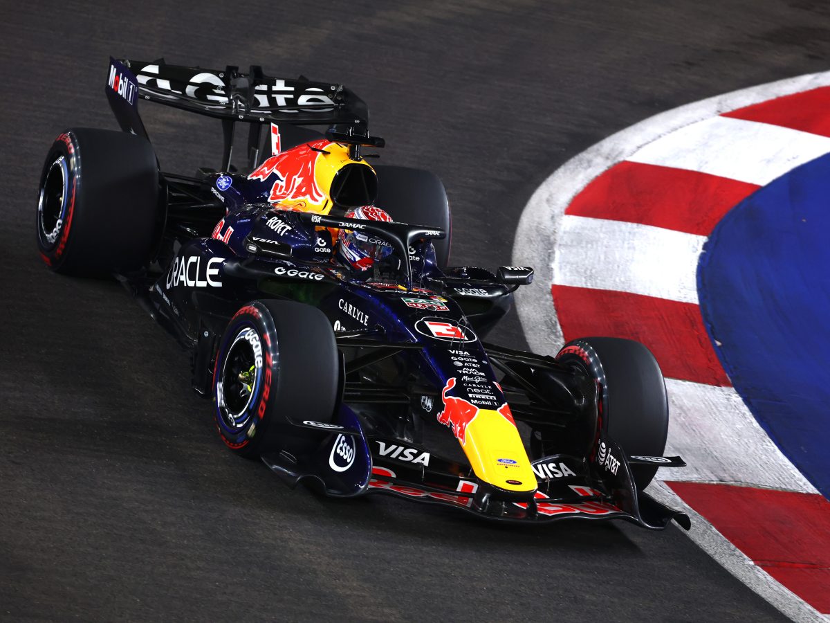 Overhead view of Max Verstappen's dark blue Oracle Red Bull Racing Formula 1 car negotiating a corner beside red-and-white kerbs and blue run-off at the floodlit Marina Bay Street Circuit in Singapore.